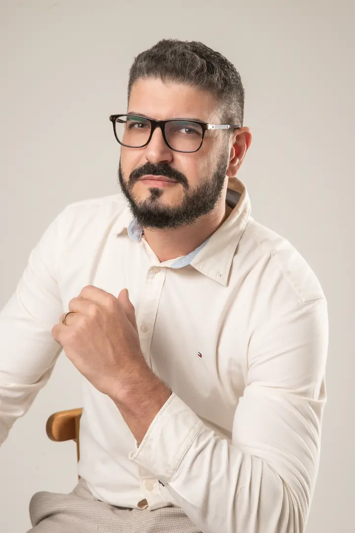 Dr. Emerson Cruz, de camisa clara e óculos, sentado, olhando para a câmera